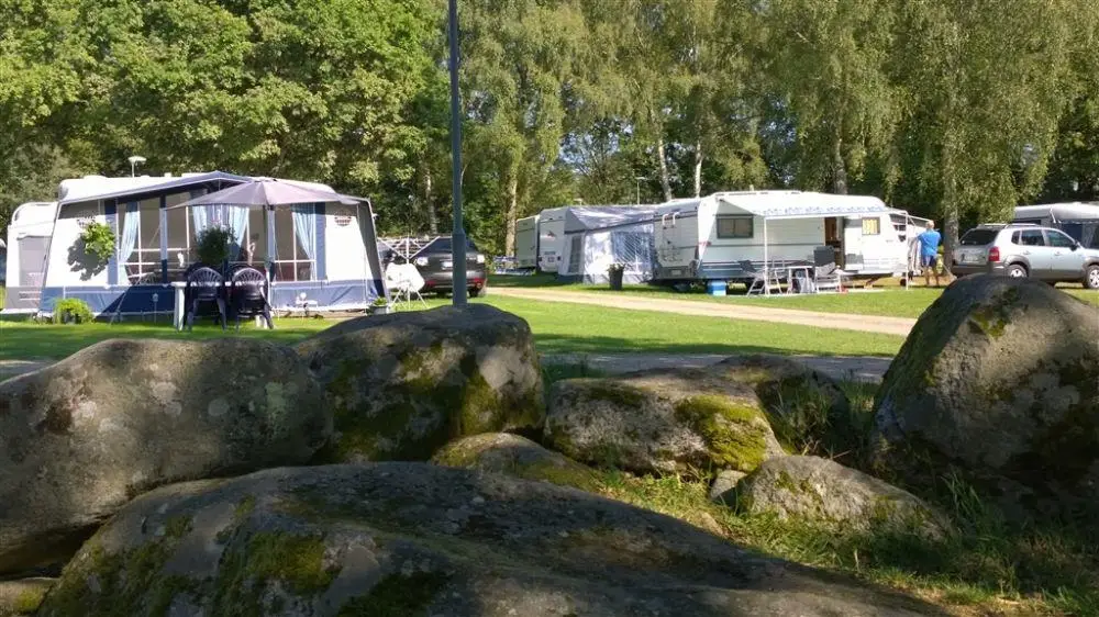 En naturskön bild av Långasjönäs Camping & Stugby, omgiven av frodiga gröna träd. Människor njuter av fritidsaktiviteter i den lugna parken. En perfekt plats för avkopplande semester.
