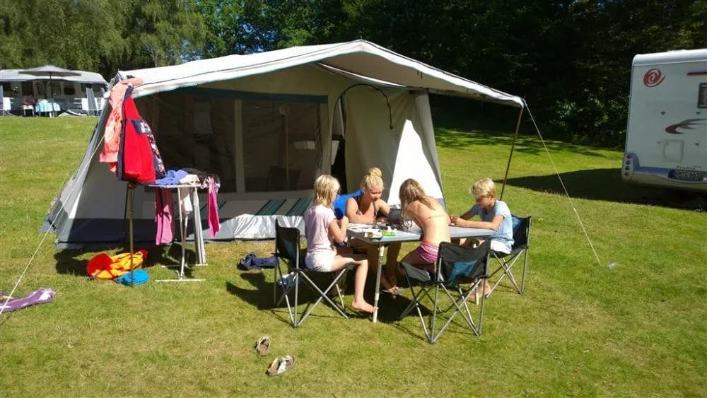 En campingplats omgiven av grönska med husvagnar, utomhusbord, stolar och vikbara stolar, som skapar en inbjudande och avslappnande atmosfär vid Långasjönäs camping & stugby.