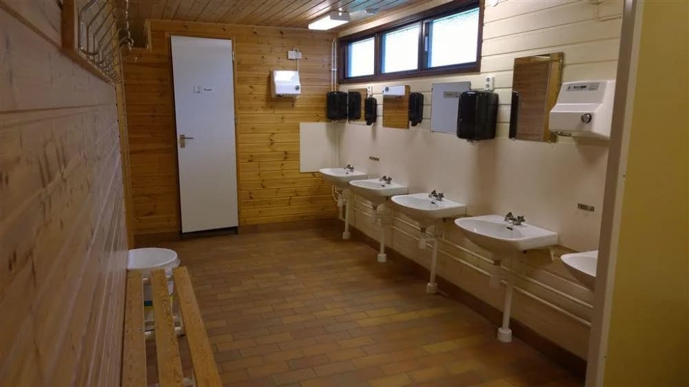 En modern och stilren badrumsinteriör med trägolv och väggar, ett handfat i vitt porslin och blandare i metall vid Långasjönäs camping & stugby.