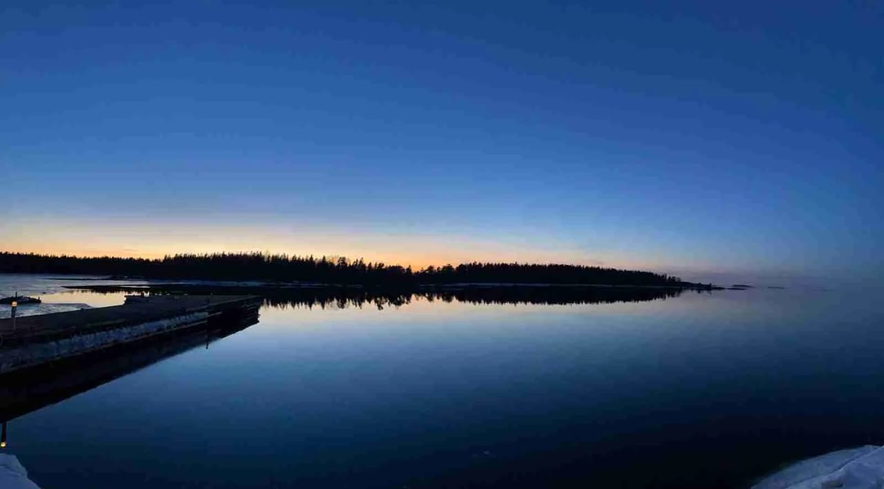 En vacker kustvy vid skymningen över en hamncamping i Ängskär, där det lugna vattnet reflekterar den blå horisonten och skapar en rogivande atmosfär.