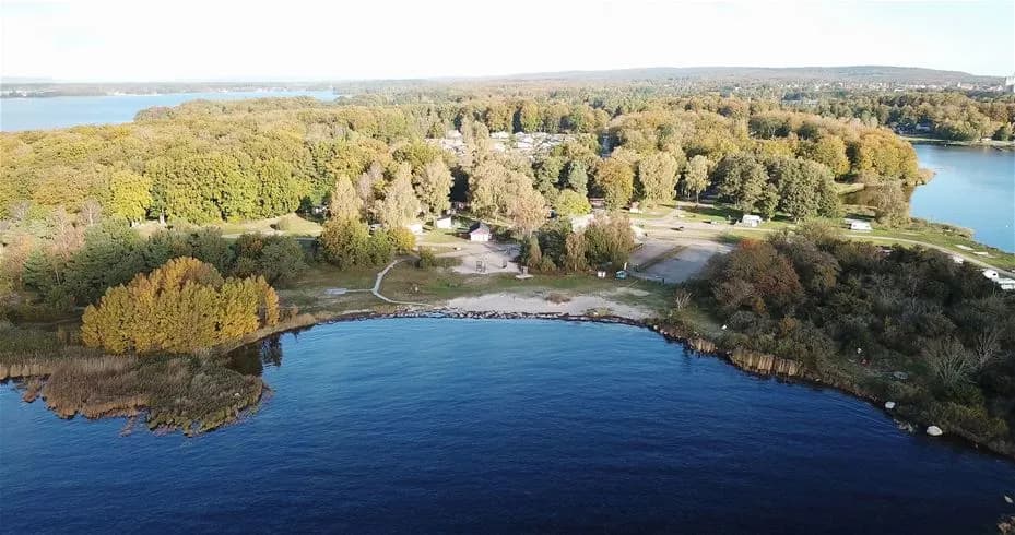 Flygfoto över ett kustlandskap vid My Camping Tredenborg, där strandlinjen sträcker sig längs ett vattenområde med lugna blåa toner.