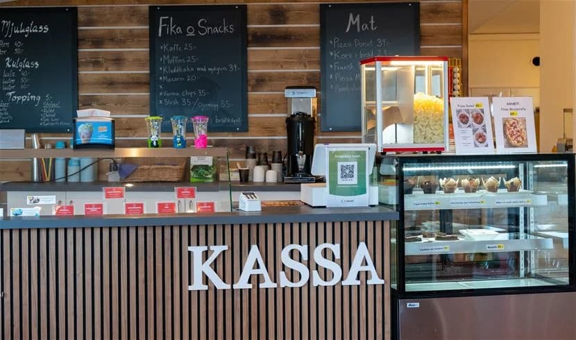 Bild av en matservering på My Camping Tredenborg, med fokus på snabbmat och bageriprodukter. Flera matvaror är synliga tillsammans med delar av en restaurangmiljö.