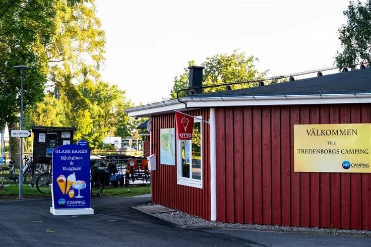 En skuggig allmän plats med en reklampelare i förgrunden på my camping Tredenborg.