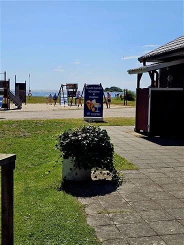 Campingplats med grönytor och trädbeklädd skugga, utrustad med utomhusmöbler och bänkar för rekreation och avkoppling.