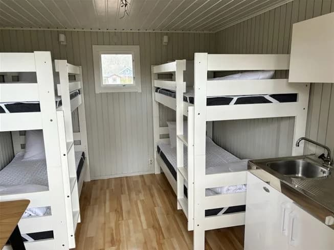 En träfylld sovsal med våningssängar, träpaneler och en dörr, typisk för ett campingställe som My Camping Tredenborg.