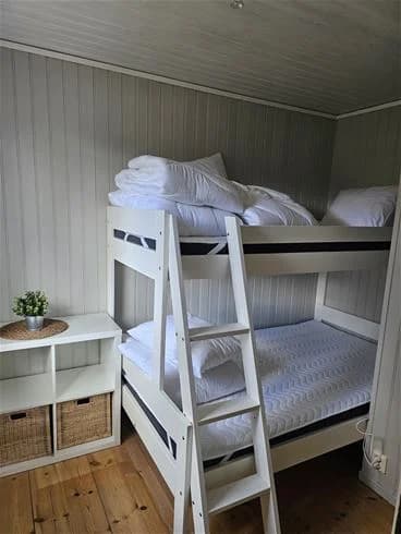 Ett sovrum med två våningssängar i trä, ljusa trägolv och enkla sängkläder, inredningen är funktionell och hemtrevlig.