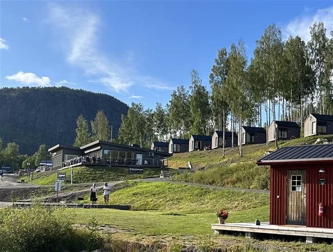 En naturskön vy över Skuleberget Havscamping med stugor utspridda i ett lantligt landskap, omgiven av böljande kullar och en bergskedja i bakgrunden.