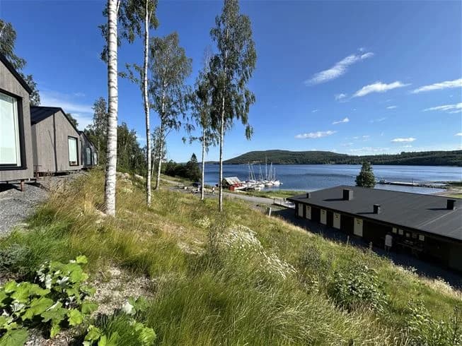 En liten stuga vid en sjö omgiven av grönskande landskap, med ett berg i bakgrunden på Skuleberget Havscamping.