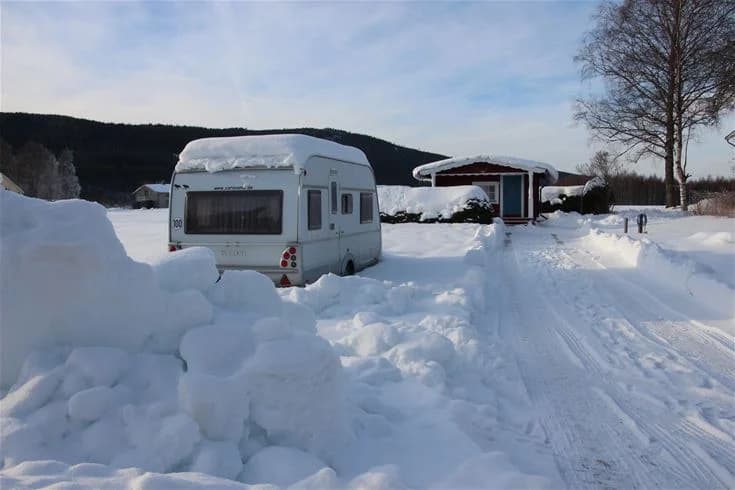 En husbil parkerad på en snötäckt campingplats på Björkebo camping, omgiven av ett vintrigt landskap med snöfall och is.