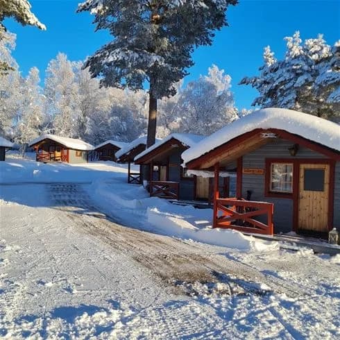 En trästuga täckt av snö i ett vinterlandskap, belägen på Sonfjällscampen.