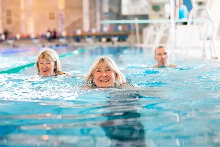 En grupp människor njuter av en simtur i poolen på Fyrishov stugby och camping, omgivna av skratt och leenden i en avslappnad och glad atmosfär.