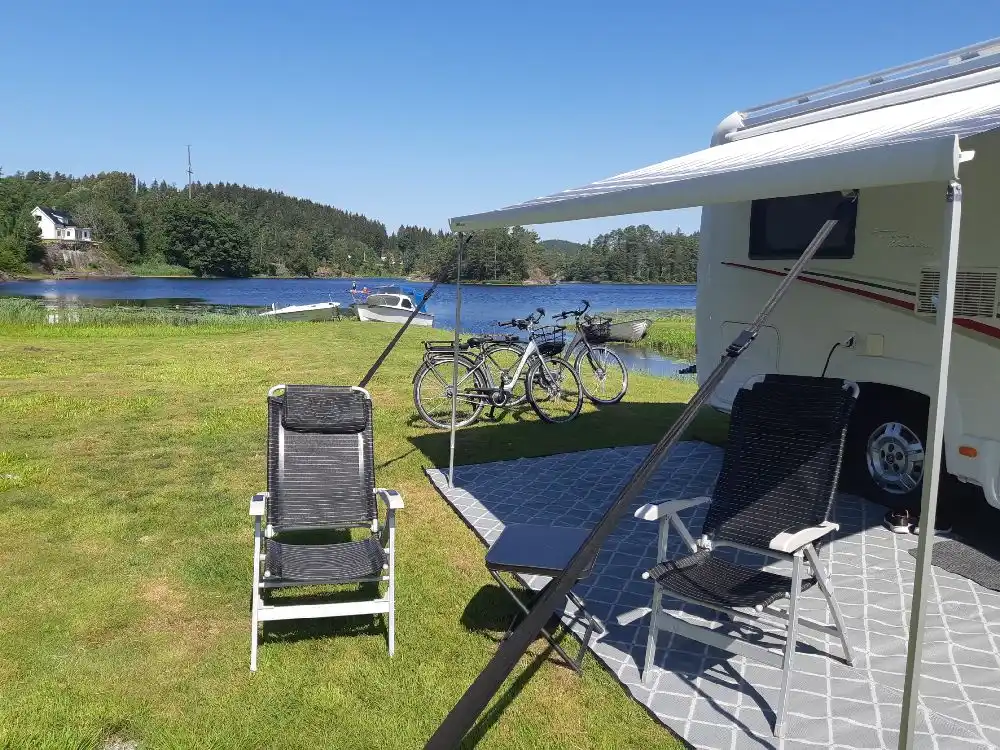 En campingplats med flera husvagnar och husbilar uppställda bland grönska. Utomhusmöbler är placerade i närheten för rekreation och avkoppling.