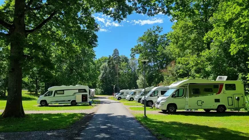 En grönskande camping i Trollhättan med uppställda husvagnar och husbilar, parkerade cyklar och en luftig parkmiljö.