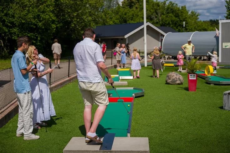 En grön och livlig campingplats i Trollhättan med konstgräs, där besökare kan njuta av utomhusaktiviteter och spel i en offentlig och avslappnad miljö.