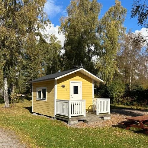 Färgglada sommarstugor omgivna av välskötta gräsmattor och trädgårdsbyggnader på Alholmens camping.