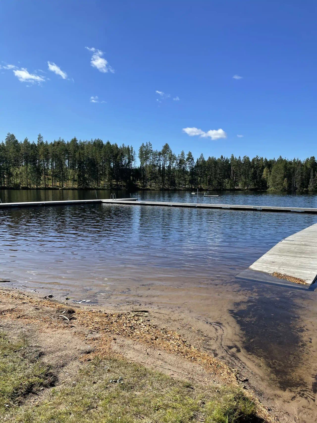 En naturskön vy över en sjö med spegelblankt vatten, omgiven av frodiga bankar och öppna våtmarker, nära Liens camping.