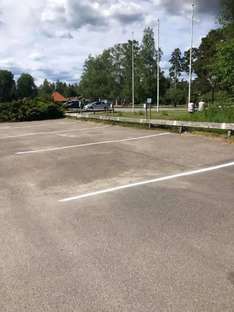 En asfalterad parkeringsplats vid Målerås Glasbruk med flera parkerade bilar, bland annat familjebilar och lyxbilar.