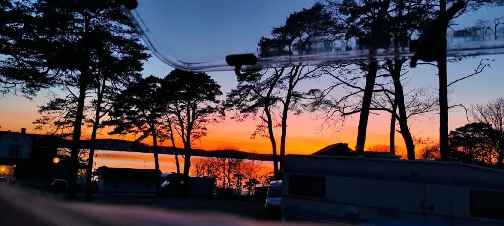 En vacker solnedgång över Stenungsögården med himlen i mjuka orange och rosa färger, som speglas i det stilla vattnet.