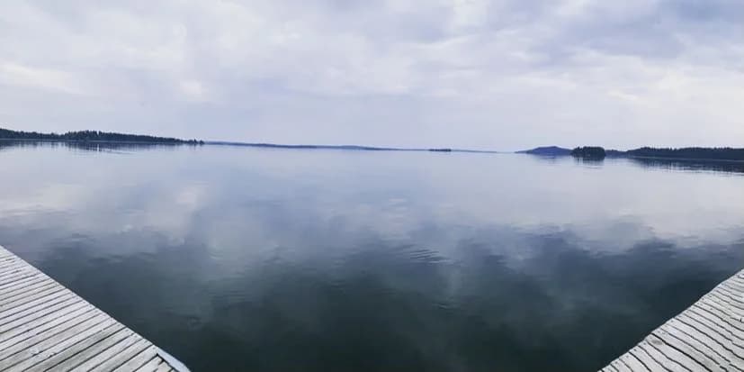 En klarblå himmel speglas i en fridfull sjö vid Björknäs camping, omgiven av gröna skogar under en molnfri dag.