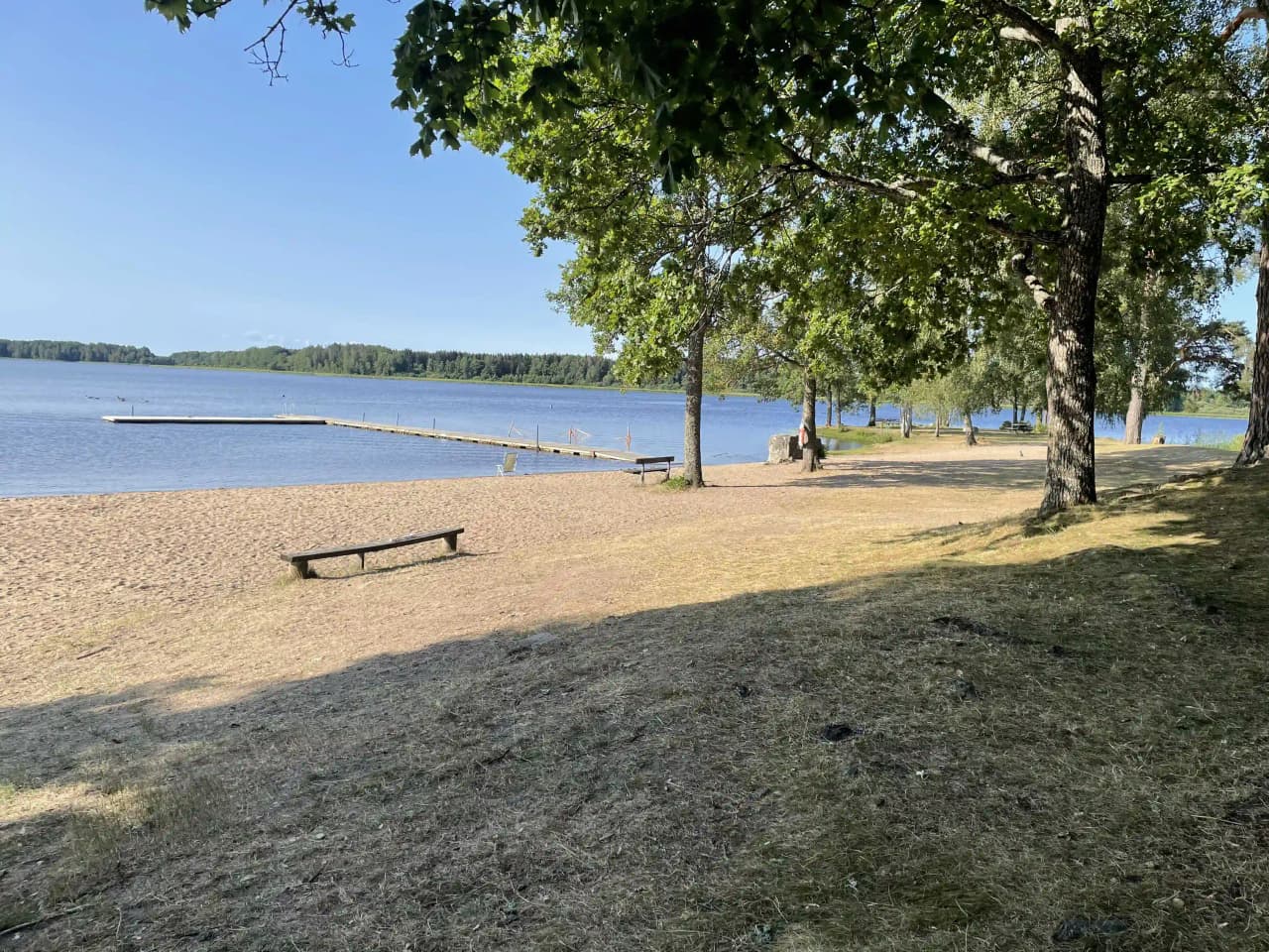 En rofylld vy över en sjö vid Prästryggens camping, med en klar horisont och gröna strandkanter.