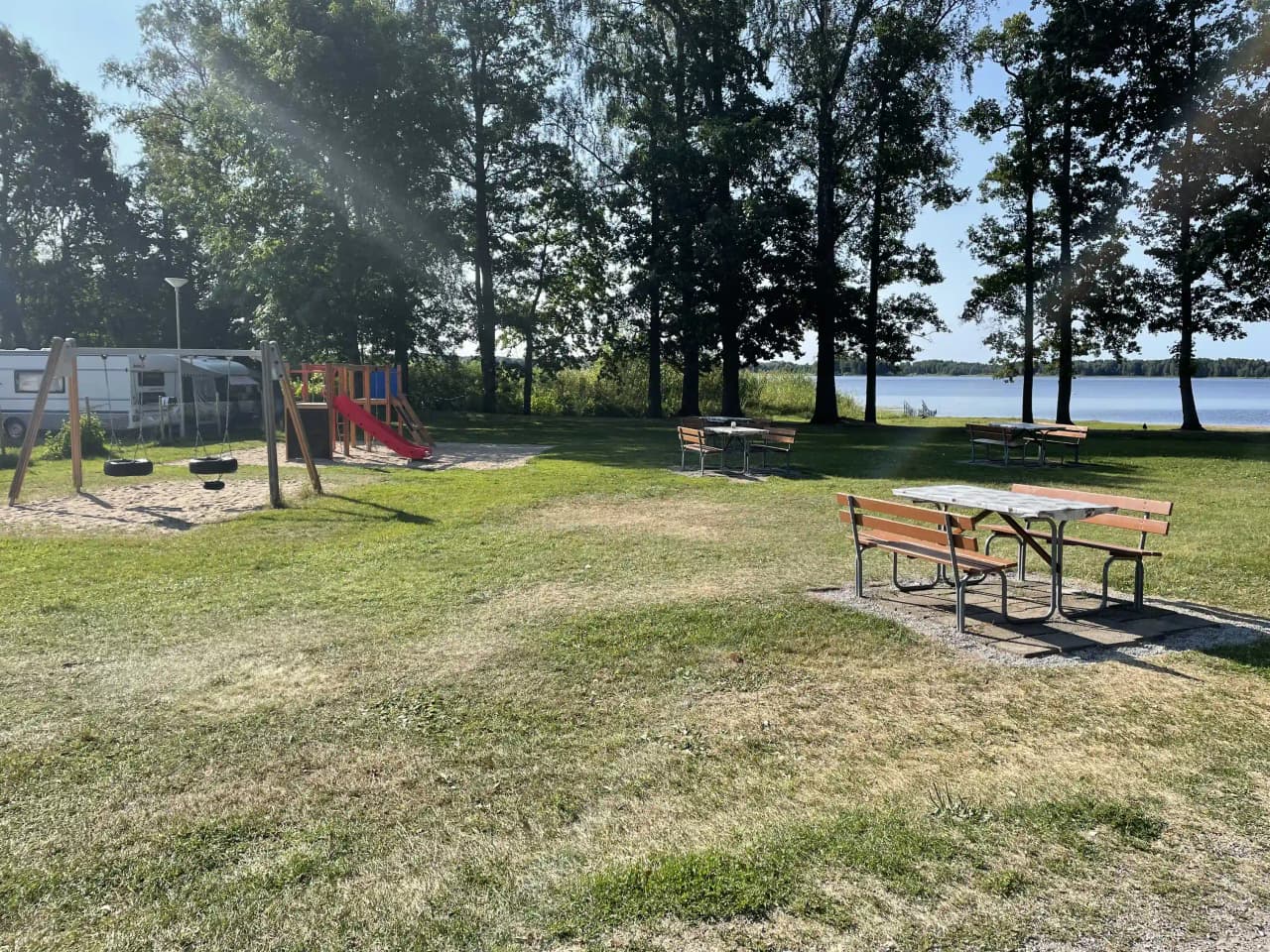 En grön gräsplan på Prästryggens camping med picknickbord och utemöbler under skugga, perfekt för avkopplande utomhusvistelser.