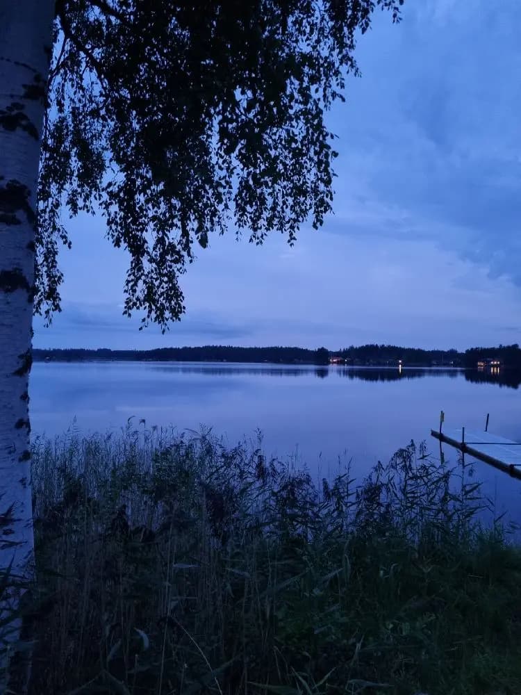 Vy över en klarblå sjö med omgivande grönska och reflektioner i vattnet vid Högbacka camping.