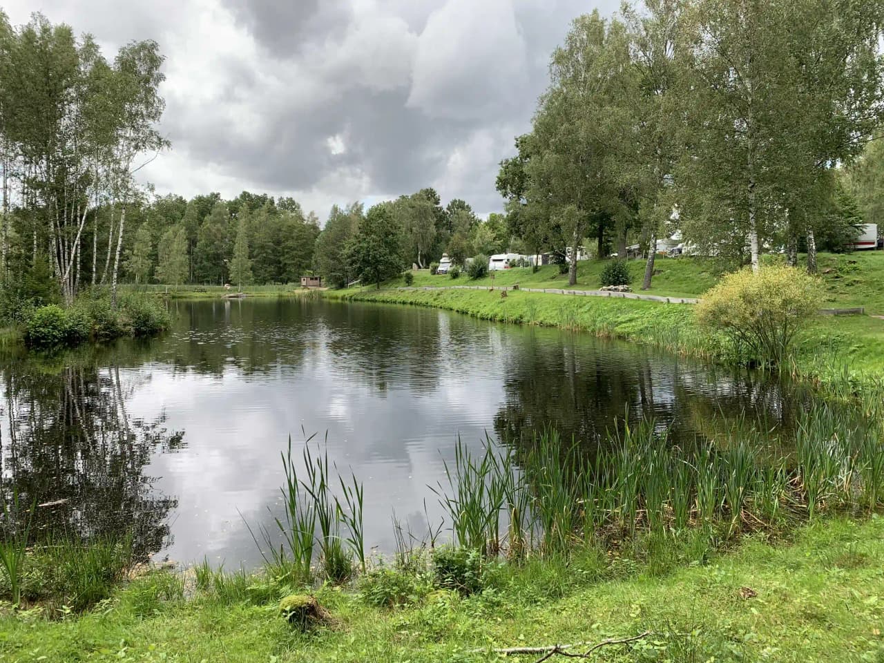 En lugn och naturskön miljö vid Våxtorps naturcamping, med en stilla vattenyta omgiven av träd och grönska.