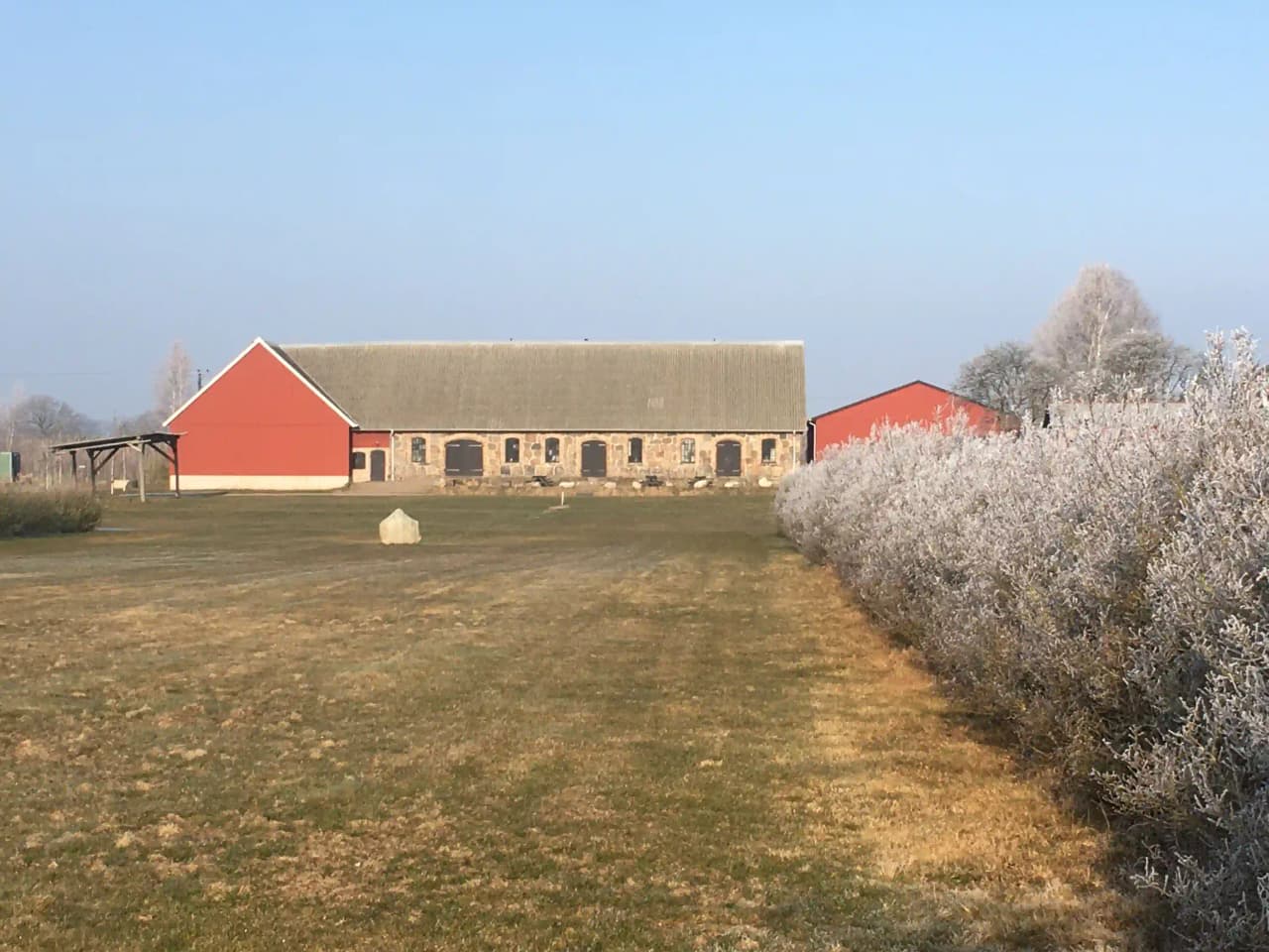 En vy över den lantliga Bläsinge gård, med gräsbevuxna fält och en lada i bakgrunden.