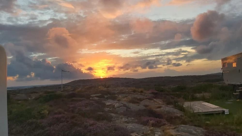 En vacker landskapsbild vid Sotenäs camping, som visar en vidsträckt horisont och en himmel i skiftande färger vid solnedgången. Moln sveper över himlen i en naturskön och lantlig miljö.