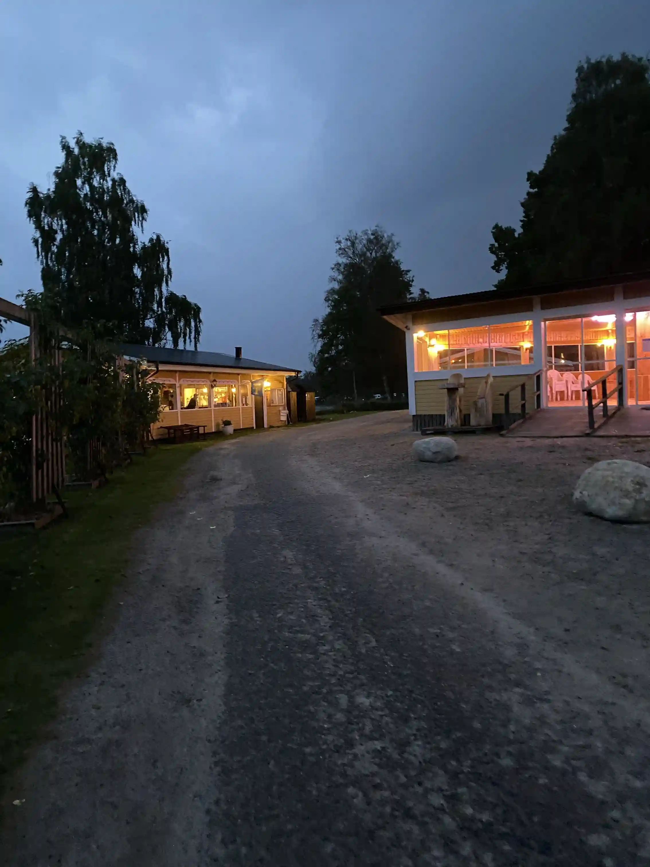 En skuggig gårdsplan med uppfart vid Ljuvadal Camping & Ställplats, omgiven av utomhusstrukturer och en mysig atmosfär i kvällsljus.