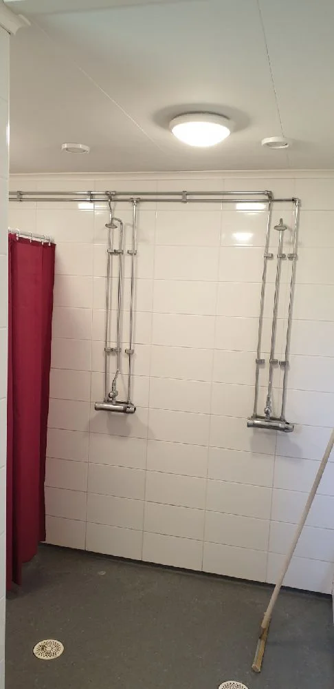 Inne i ett modernt badrum med silverfärgade VVS-armaturer, vita kakelplattor och diskret belysning. Taket och golvet är prydligt och stilrent.