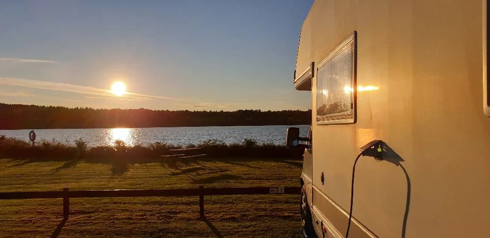 En solnedgång över Målsånna Camping Park med husbilar och husvagnar i förgrunden, omgivna av ett mjukt efterglödande ljus.