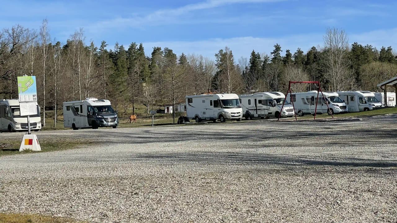 En husbil och en van parkerade i Upperuds Gästhamns parkeringsområde, med träd i bakgrunden och asfalt under fordonen.