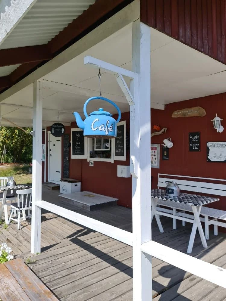 Alt-text: En trädäckad veranda på Säms camping och café med utemöbler under ett skuggande tak.