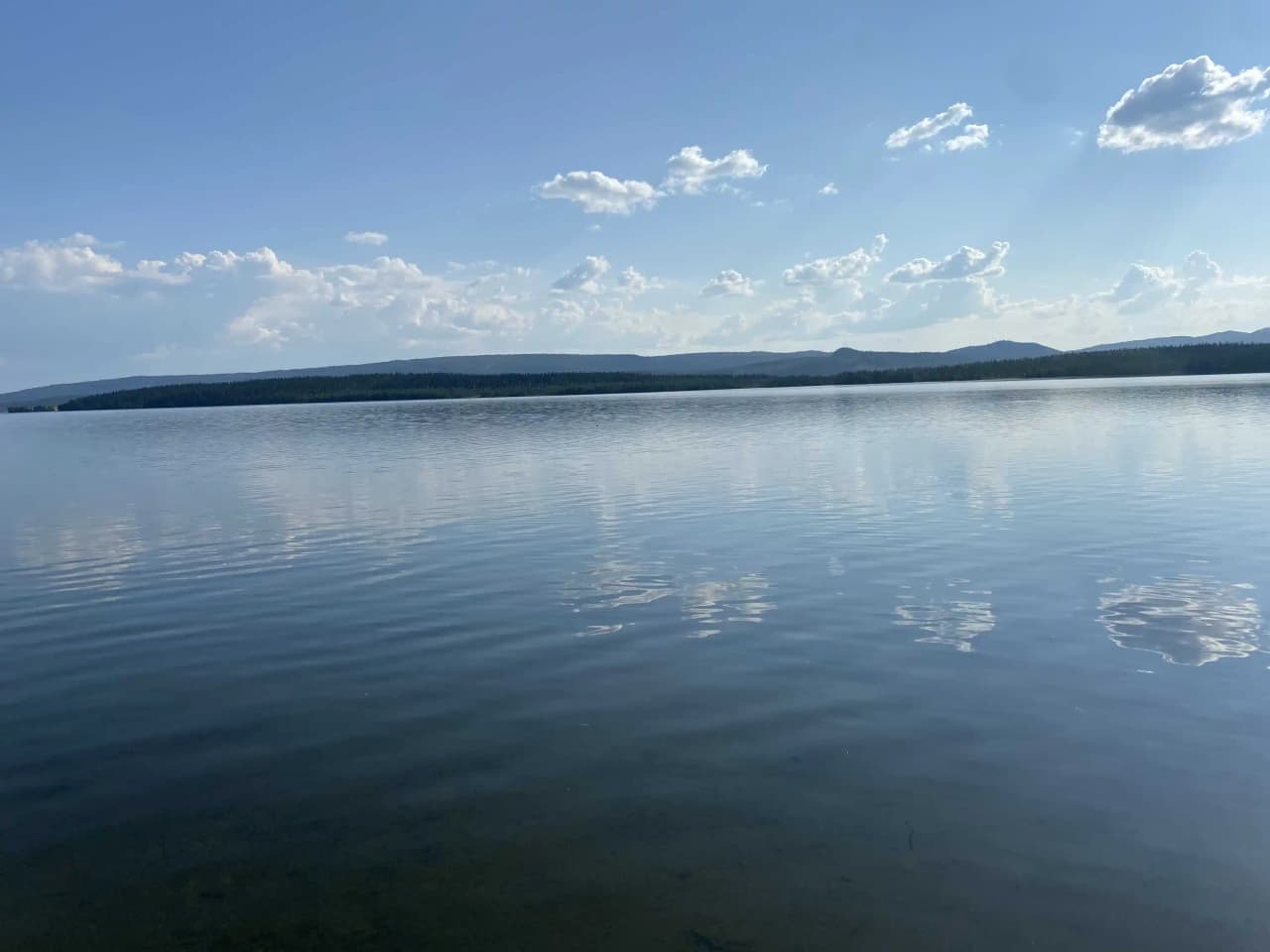 Bild av Jormvattnets Fiskecamp med klar blå himmel och vita moln. Ett vidsträckt vattendrag syns i förgrunden, med horisonten i fjärran.