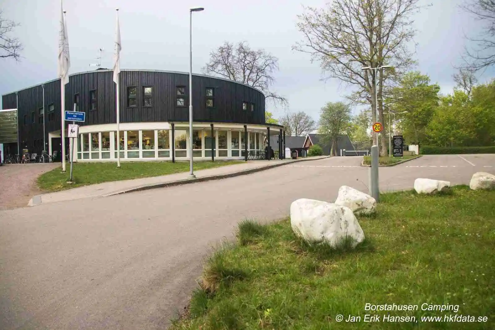 En öppen offentlig yta vid mötesplats Borstahusen med skuggiga områden, stolpar och en välskött gård, omgiven av moderna byggnader som ger en känsla av ett gemenskapscentrum eller ett företags huvudkontor.
