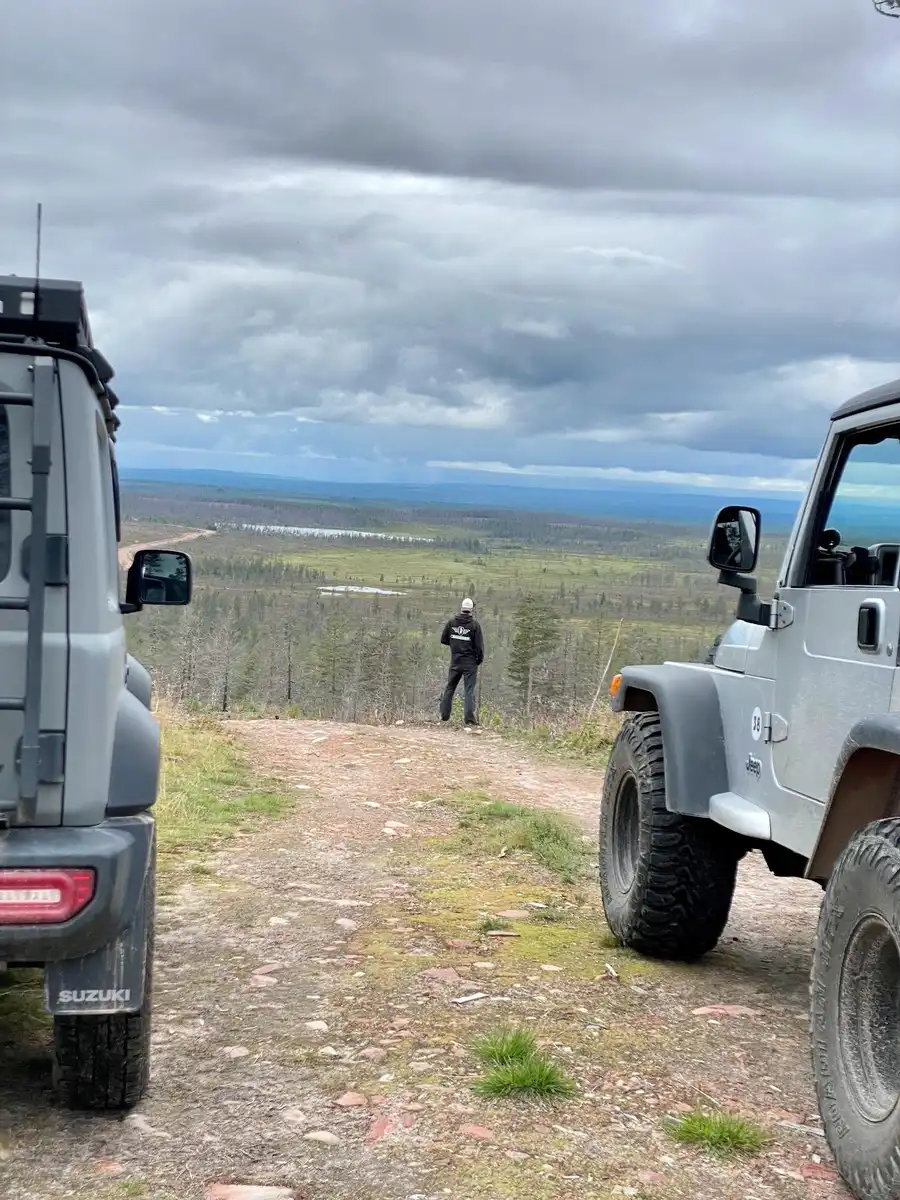 En terrängfordon med kraftiga däck kör genom en lerig bana, omgiven av grönska. Fordonet är utrustat för offroad-äventyr, vilket gör det lämpligt för utomhusaktiviteter och resor i tuff terräng.