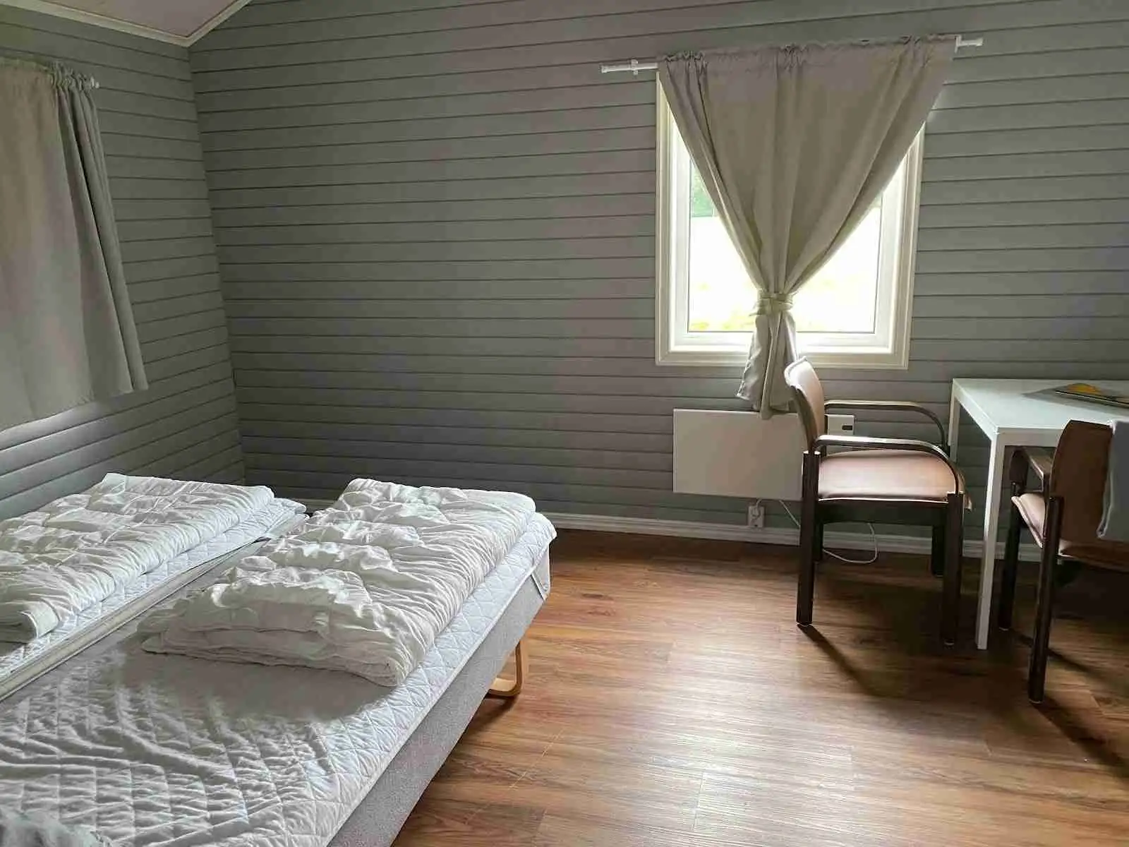 Interiörbild av en trästuga med ett sovrum, trägolv och trätak. Rummet har en varm och inbjudande atmosfär med träpaneler på väggarna och möbler i rustikt trä.