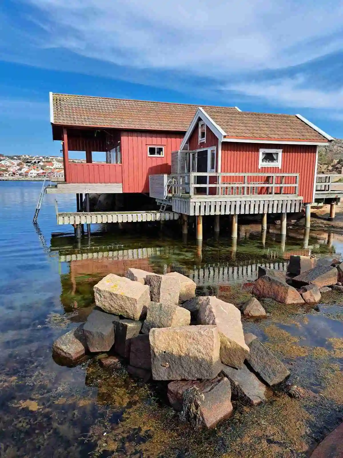En idyllisk vy över Hunnebostrands camping och stugor med små stugor i trä nära vattenbrynet, omgivna av frodig natur och en vacker kustlinje.