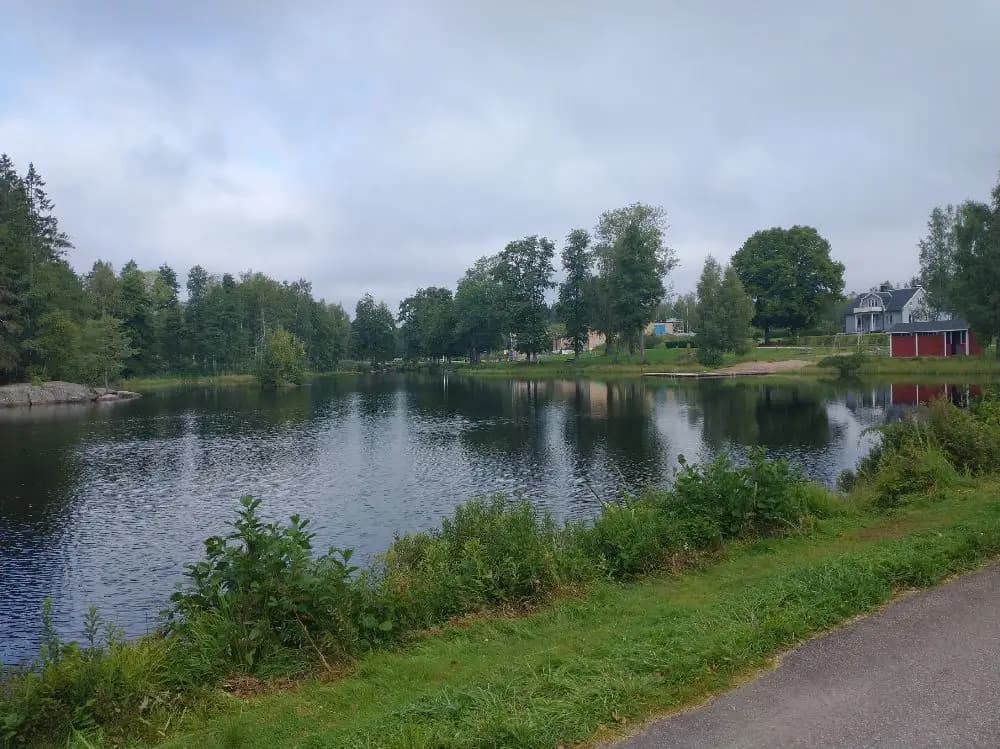 En lugn vattenyta omgiven av frodig grönska, med träd som speglas i vattnet vid Broakulla Ställplats & Camping.