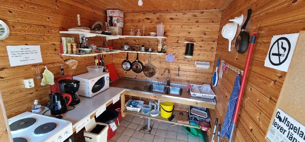 En träinredd interiör på Bjurholms camping. Rummet har golv och hyllor av trä, möbler och förvaringsskåp av trä, samt synliga köksdetaljer.