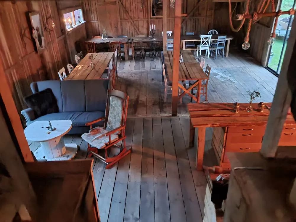 En lantlig och rustik interiör med träbord och stolar på trägolv. Taket och omgivningen är också inredda i trä, vilket ger en varm och inbjudande atmosfär.