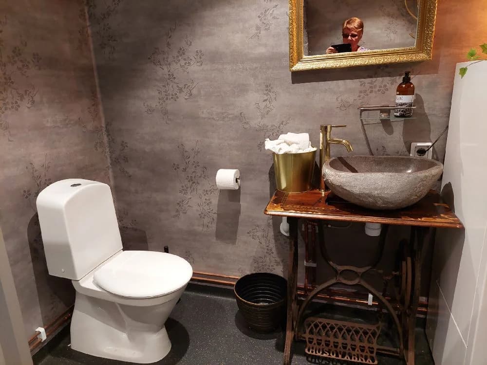 Ett stilrent badrum med ett vitt porslinstoalett, en toalettsits och moderna VVS-element. Rummet har kaklade väggar och detaljer i keramik, vilket ger en ren och funktionell interiördesign.