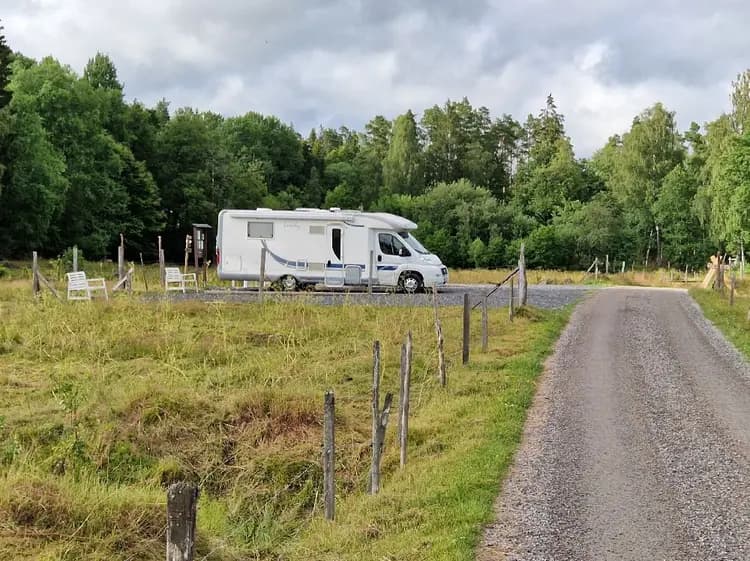 En husvagn står uppställd på en naturskön plats vid Stjernkvist’s Hunshult, omgiven av gröna träd och blå himmel.