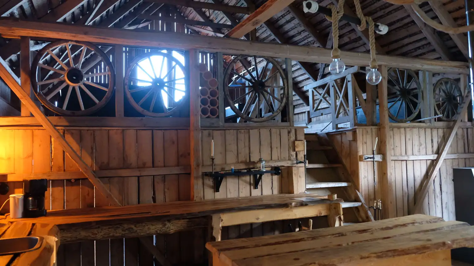 Interiör av en rustik byggnad med trädetaljer, inklusive synliga takbjälkar, plankor och paneler. Ljusa träslag ger en varm och inbjudande atmosfär, med fokus på naturligt material och hantverk.