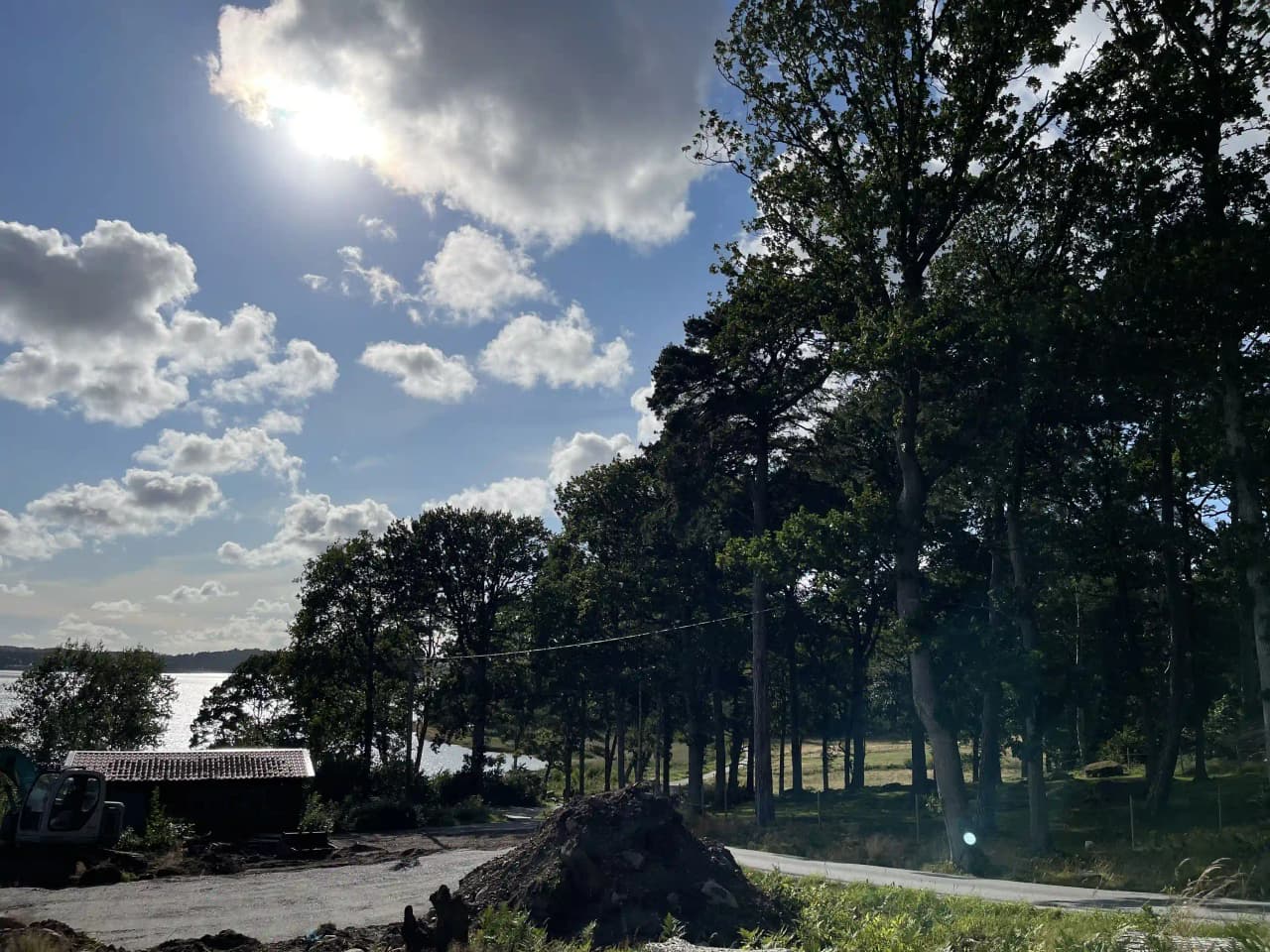 En vy över ett naturskönt område vid Stenungsögården med blå himmel, vita moln och frodig grönska. Träd och växtlighet ramar in landskapet under molnformationerna.