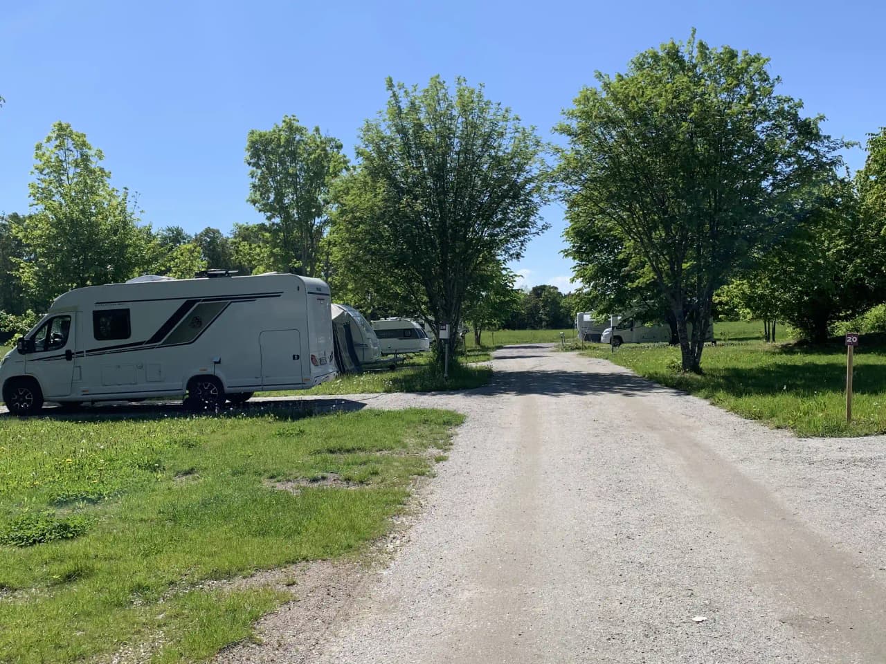En husvagn och en husbil parkerade på en asfalterad infart vid Björknäs camping, med träd och grönska i bakgrunden.
