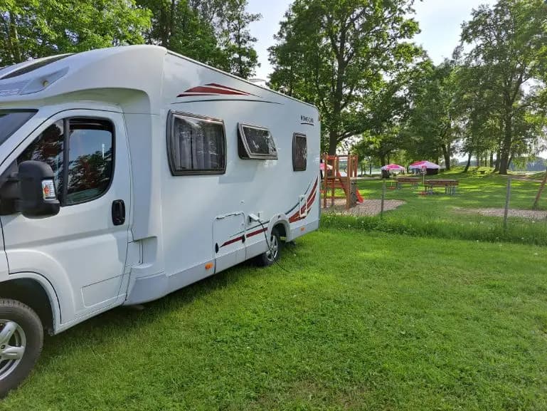 En husvagn och en husbil parkerade på en campingplats med öppna dörrar, omgivna av grönska.