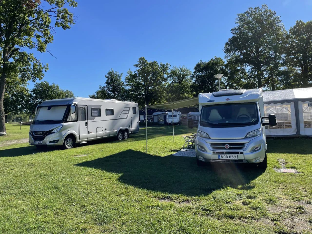En husbil står parkerad vid Prästryggens camping, omgiven av skog och natur. Flera campingvagnar syns i bakgrunden, vilket ger en känsla av gemenskap och friluftsliv.