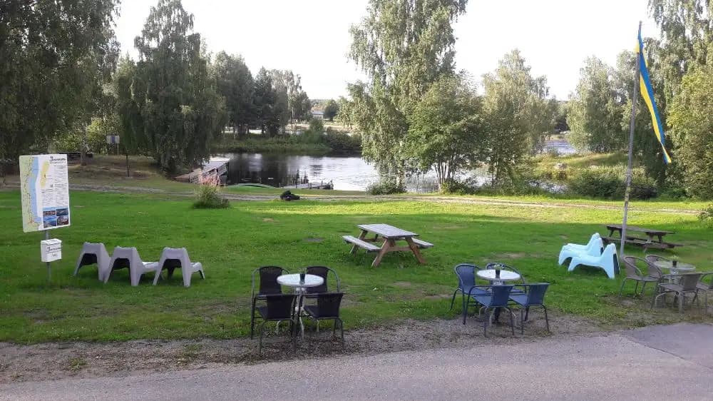 En grönskande campingplats med utomhusmöbler, inklusive bord och bänkar, placerade på en välskött gräsmatta.